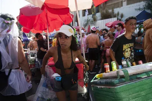 A vendor pulls through a crowd of revelers a cart carrying a cooler of ice cold beverages at the Heaven on Earth pre-Carnival street party, in Rio de Janeiro, Saturday, Feb. 22, 2025. (AP Photo/Bruna Prado)