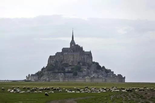 Sheeps graze in the fields around the Mont Saint Michel, Wednesday, May 8, 2018, in western France. France’s beloved abbey of Mont-Saint-Michel has reached a ripe old age. It's been 1,000 years since the laying of its first stone. The millennial of the UNESCO World Heritage site and key Normandy tourism magnet is being celebrated until November with exhibits, dance shows and concerts. French President Emmanuel Macron is heading there on Monday, June 5, 2023. (AP Photo/Thibault Camus, File)