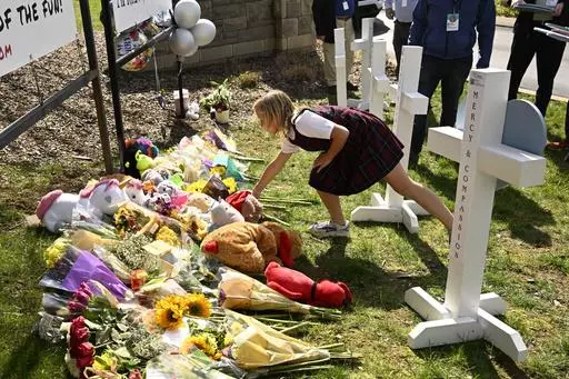 A young girl places an item at a growing memorial,Tuesday, March 28, 2023, in Nashville, at an entry to Covenant School for the victims of Monday' shooting. (AP Photo/John Amis)
