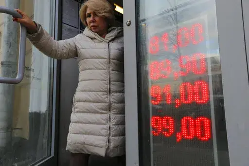 In this Feb. 24, 2022, photo, a woman leaves an exchange office with screen showing the currency exchange rates of U.S. Dollar and Euro to Russian Rubles in Moscow, Russia. The harsh sanctions imposed on Russia and the resulting crash of the ruble have the Kremlin scrambling to keep the country's economy running. For Russian President Vladimir Putin, that means finding workarounds to the economic blockade even as his forces continue to invade Ukraine. (AP Photo/Alexander Zemlianichenko Jr., File