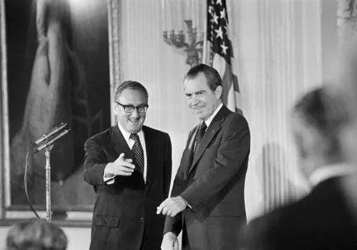 Secretary of State Henry Kissinger, left, gestures to the audience in the East Room of the White House, Sept. 22, 1973, as President Richard Nixon watches, in Washington. Kissinger had just been sworn in as the 56th secretary of state. Kissinger, the diplomat with the thick glasses and gravelly voice who dominated foreign policy as the United States extricated itself from Vietnam and broke down barriers with China, died Wednesday, Nov. 29, 2023. He was 100. (AP Photo, File)