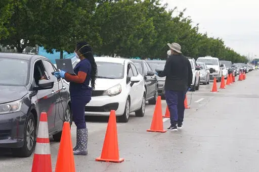 Employees of Nomi Health check in a long line of people for COVID-19 tests, Tuesday, Dec. 21, 2021, in North Miami, Fla. The omicron variant has unleashed a fresh round of fear and uncertainty, for travelers, shoppers and party-goers around the U.S. (AP Photo/Marta Lavandier)