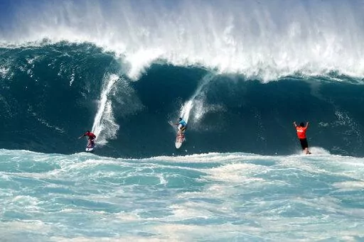 Kai Lenny, left, and Aaron Gold, center, are cheered on by Jake Maki, right, in Hawaii's Waimea Bay on Oahu’s North Shore during the The Eddie Aikau Big Wave Invitational surfing contest Sunday, Jan. 22, 2023. (Jamm Aquino/Honolulu Star-Advertiser via AP)