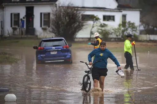 Siquoia Jackson, of Huntington, pulls a bike through the floodwater while trying to travel through the Enslow Park neighborhood on Thursday, Feb. 6, 2025, in Huntington, W.Va. (Ryan Fischer/The Herald-Dispatch via AP)