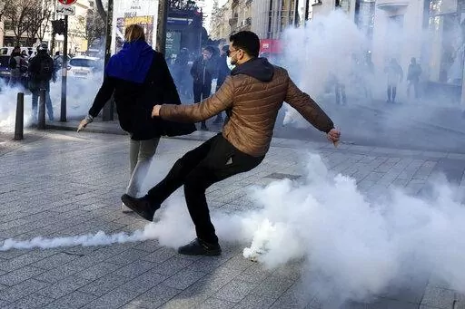 A demonstrator kicks in a tear gas grenade during a protest on the Champs-Elysees avenue, Saturday, Feb.12, 2022 in Paris. Paris police intercepted at least 500 vehicles attempting to enter the French capital in defiance of a police order to take part in protests against virus restrictions inspired by the Canada's horn-honking "Freedom Convoy." . (AP Photo/Adrienne Surprenant)