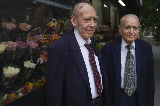 Octogenarian brothers from Ecuador, Carlos Cevallos, left, and Miguel Cevallos, together during a press meeting, Monday Aug. 29, 2022, in New York. For years the Cevallos brothers made a living drawing posters for nightclubs, taco trucks and restaurants, attracting clients by word of mouth, but an Instagram account changed a lot of that. (AP Photo/Bebeto Matthews)