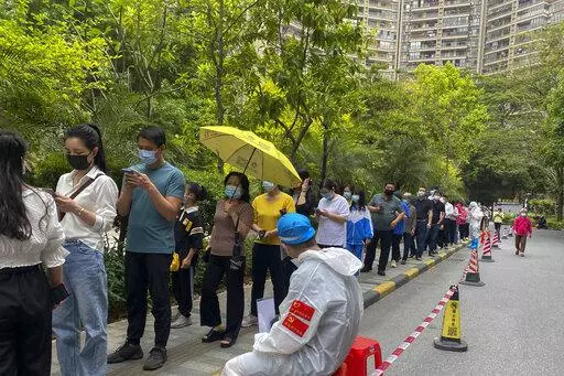 Workers in protective gear watch over residents line up for the COVID-19 test at a residential block, Monday, April 11, 2022, in Guangzhou in south China's Guangdong province. The manufacturing hub of Guangzhou began tightly restricting departures and arrivals Monday as eastern China battles the country's latest major COVID outbreak. (Chinatopix Via AP)