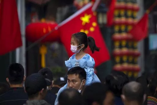 A girl wearing a face mask rides on a man's shoulders as they walk along a tourist shopping street in Beijing on Oct. 7, 2022. China has announced its first overall population decline in recent years amid an aging society and plunging birthrate. (AP Photo/Mark Schiefelbein, File)
