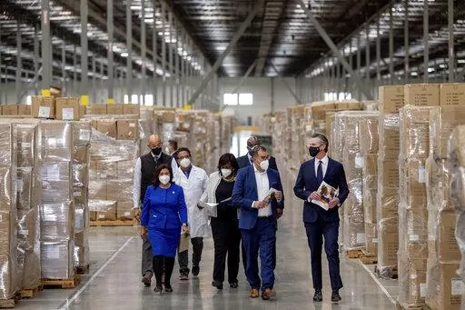Gov. Gavin Newsom, right, walks through rows of boxed Personal protective equipment, PPE, with dignitaries and elected officials, as he prepares to announce the next phase of California's COVID-19 response called "SMARTER," during a press conference at the UPS Healthcare warehouse in Fontana, Calif., on Thursday, Feb. 17, 2022. The plan is to move from the pandemic stage into an endemic stage in which people will learn to live COVID. (Watchara Phomicinda/The Orange County Register/SCNG via AP)