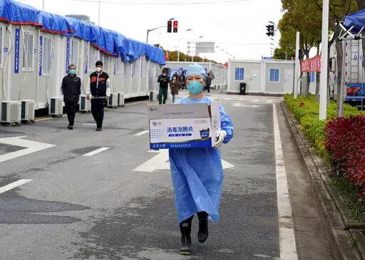 In this photo released by China's Xinhua News Agency, a worker carries a box of supplies at a makeshift hospital in Shanghai, China, Friday, April 15, 2022. Anti-virus controls that have shut down some of China's biggest cities and fueled public irritation are spreading as infections rise, hurting a weak economy and prompting warnings of possible global shockwaves. (Yang Youzong/Xinhua via AP)