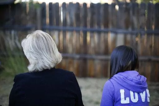 MJ and her adoptive mother sit for an interview with The Associated Press in Sierra Vista, Ariz., Oct. 27, 2021. State authorities placed MJ in foster care after learning that her father, the late Paul Adams, sexually assaulted her and posted video of the assaults on the Internet. (AP Photo/Dario Lopez-Mills)