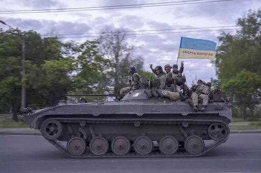 Ukrainian serviceman wave a flag with writing reading in Ukrainian "Glory to Ukraine", top, and "Death to the enemies"        as they ride atop of a tank in the Kharkiv region, eastern Ukraine, Monday, May 16, 2022. (AP Photo/Bernat Armangue)