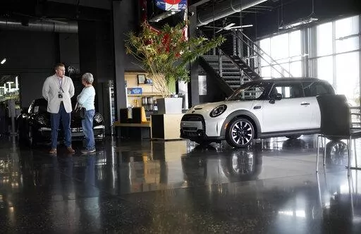 Prospective buyer chats with a sales associate as a 2022 Cooper S hardtop sits on the otherwise empty showroom floor of a Mini dealership Friday, May 6, 2022, in Highlands Ranch, Colo. As if buying a new car in today’s supply-constrained market wasn’t hard enough, this year, many shoppers are experiencing sticker shock when they realize that the car they wanted has a price tag well over the manufacturer’s suggested retail price. (AP Photo/David Zalubowski, File)