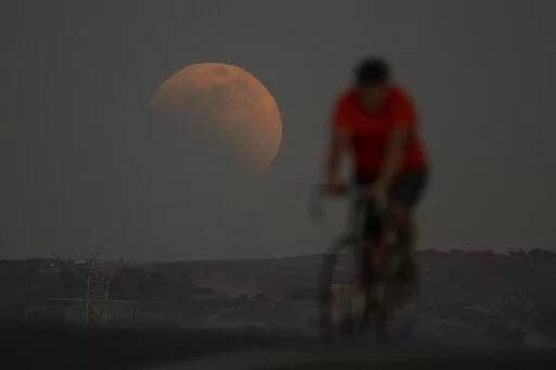 A lunar eclipse is seen behind a cyclist during the first blood moon of the year, in Irwindale, Calif., Sunday, May 15, 2022. (AP Photo/Ringo H.W. Chiu)